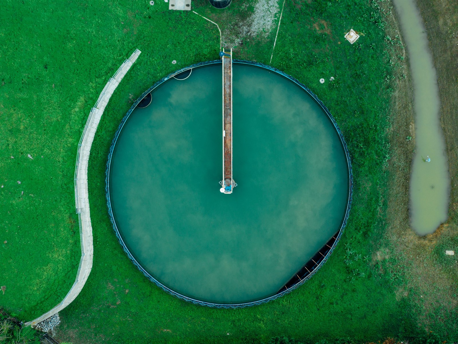 Aerial view of a large circular treatment tank set in green grassland